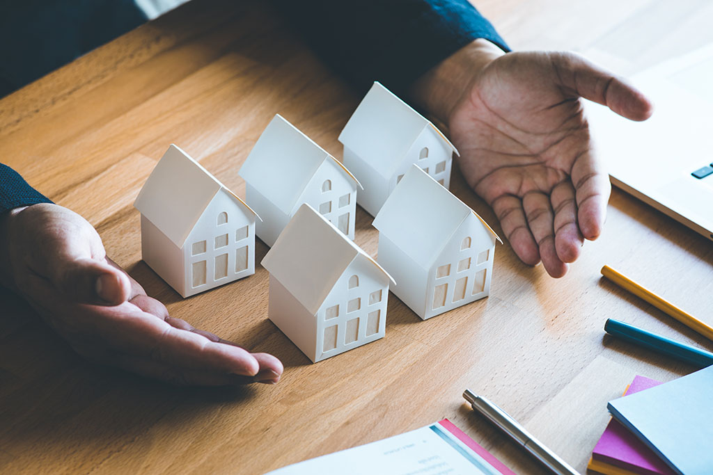 5 model homes are laid out on a table by a lender explaining how you could get 5 homes instead of 1 by using the power of a mortgage loan for leverage.  