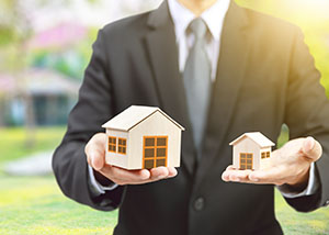 Lender holding a large house in one hand and a small house in the other to show a comparison of the type of house that would need a jumbo loan vs. the type of house that wouldn't.