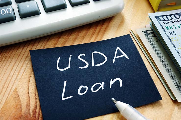 The words "USDA LOAN" written on a note on a desk next to a stack of money and a calculator