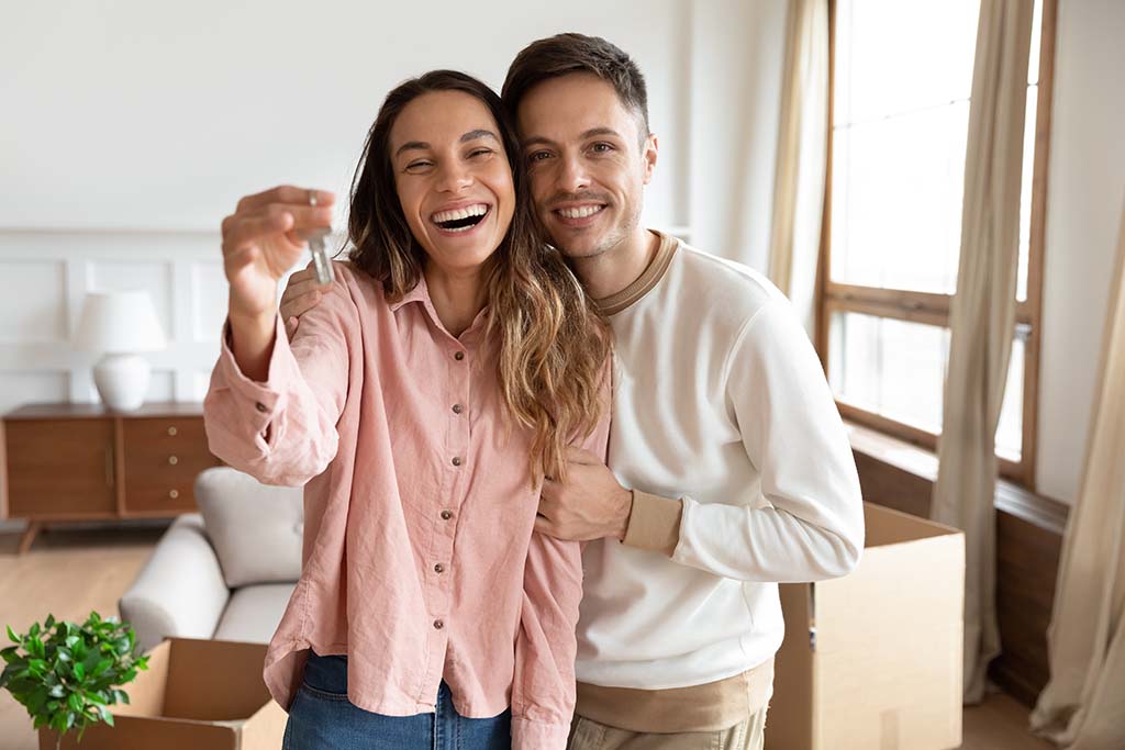 A couple, happy to be first-time homebuyers, holding up a house key and smiling.